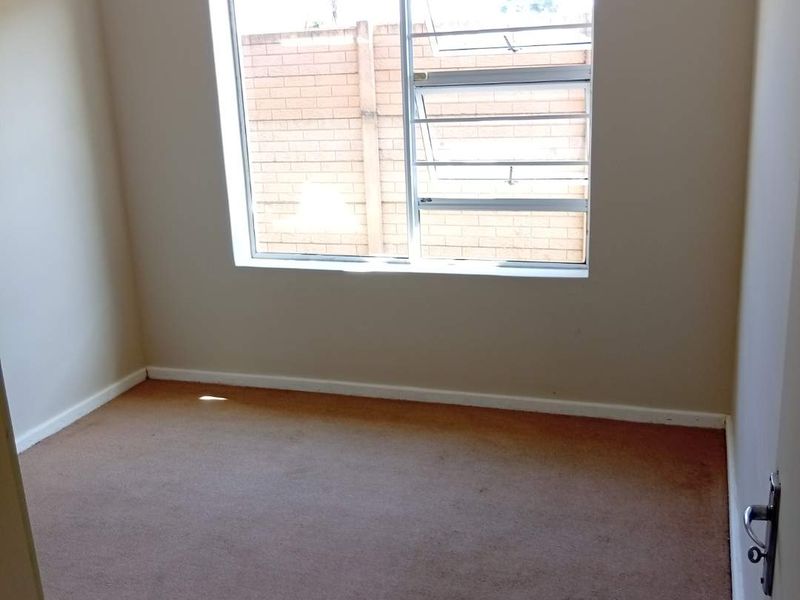 A vacant bedroom featuring neutral walls, carpeted flooring, and a window fitted with security bars.