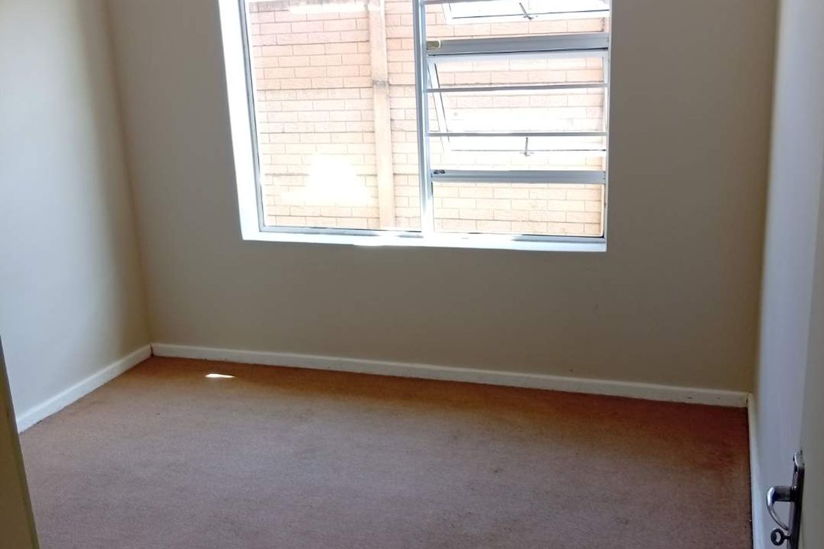 A vacant bedroom featuring neutral walls, carpeted flooring, and a window fitted with security bars.