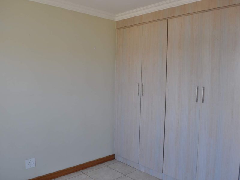 A clean, empty bedroom featuring neutral walls, tiled flooring, and ample built-in cupboard storage space.