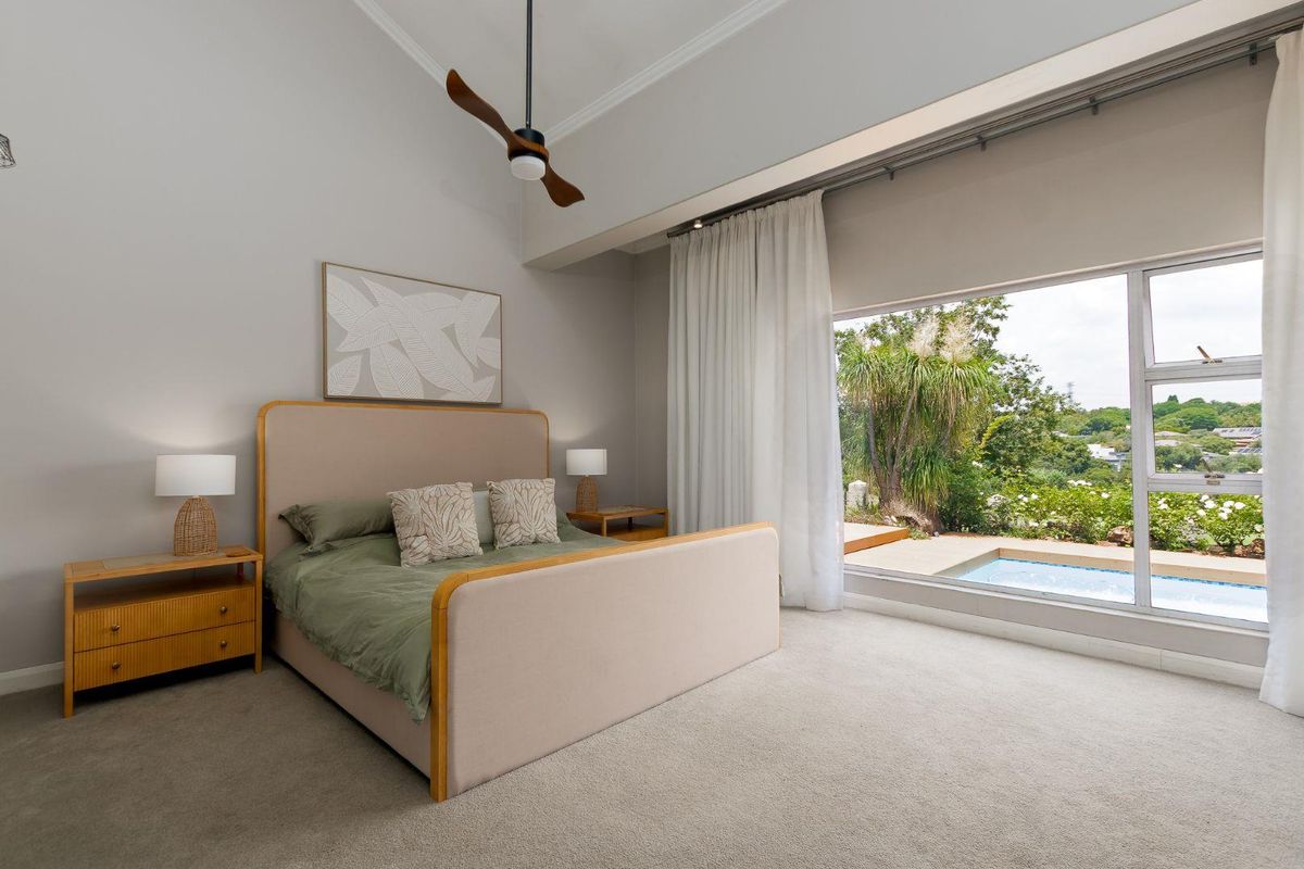 Spacious bedroom featuring high ceilings, neutral carpeting, and a large picture window offering direct views of the outdoor pool area.