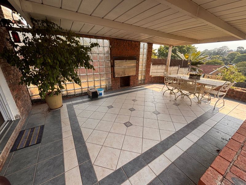 Covered outdoor patio featuring a built-in braai, decorative glass block wall, and patterned tiled flooring, ideal for alfresco dining and entertaining.