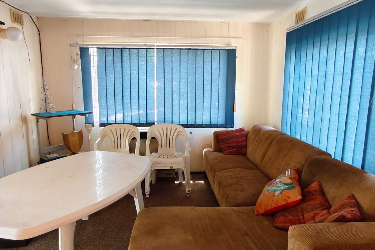 A living area featuring vertical timber wall paneling, large windows with vertical blinds, and carpeted flooring.