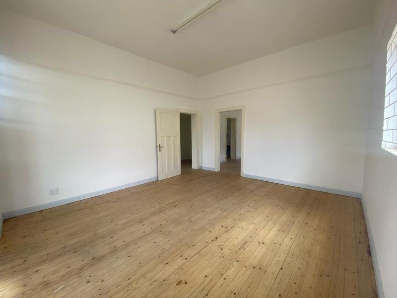 A spacious, empty bedroom featuring polished timber flooring, neutral walls, and multiple internal doorways, offering a blank canvas for interior design.
