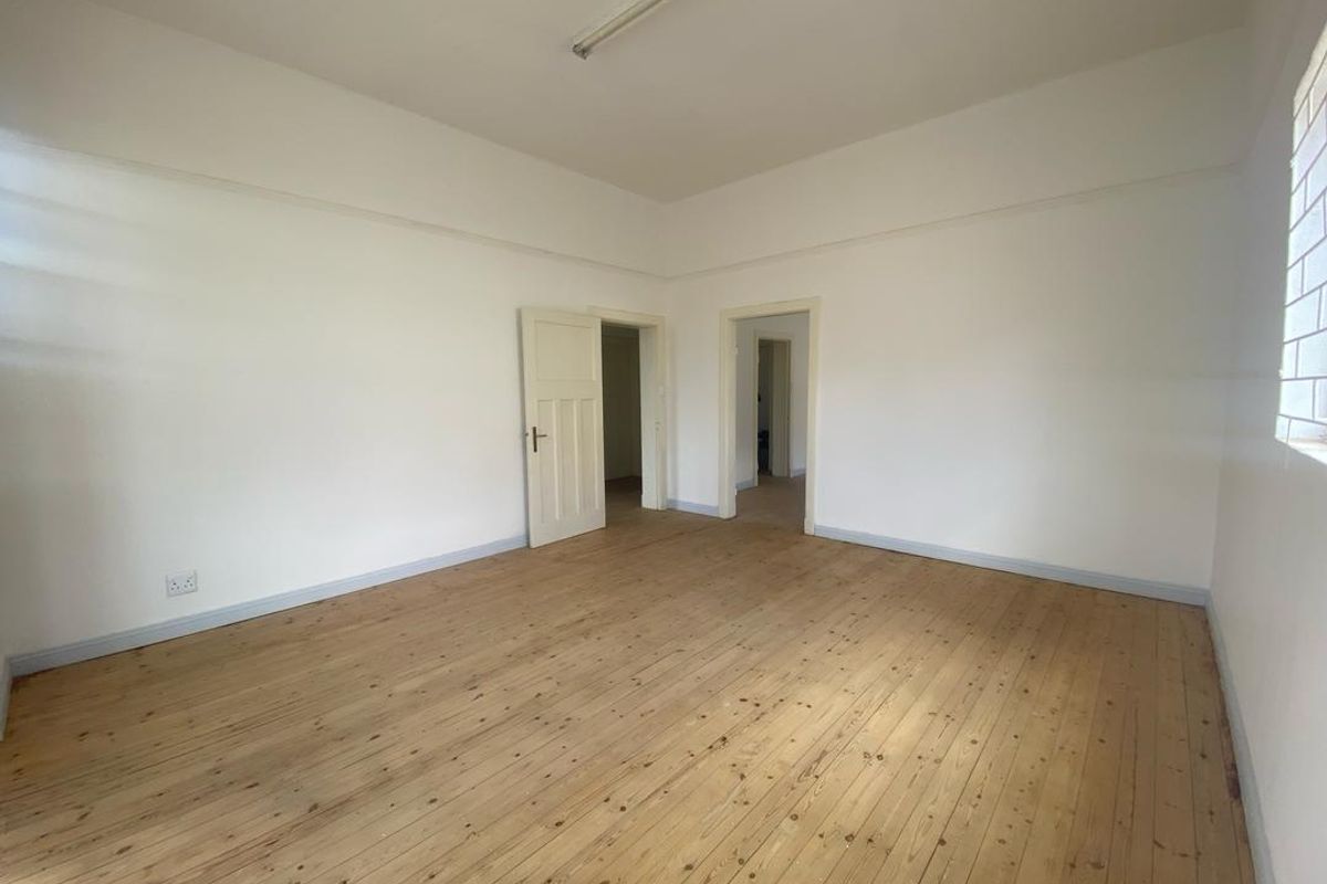 A spacious, empty bedroom featuring polished timber flooring, neutral walls, and multiple internal doorways, offering a blank canvas for interior design.