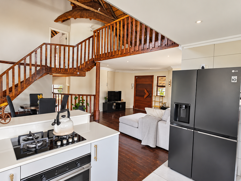 Spacious open-plan living area featuring a modern kitchen with gas hob, hardwood floors, and a striking wooden staircase leading to a mezzanine level.