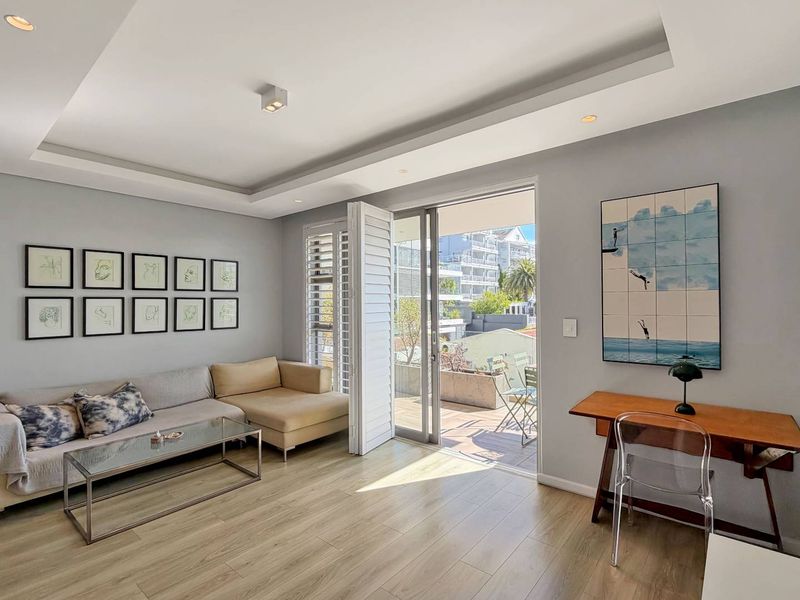 Bright living room featuring laminate flooring, recessed ceiling details, and large sliding glass doors opening onto a private balcony with plantation shutters.