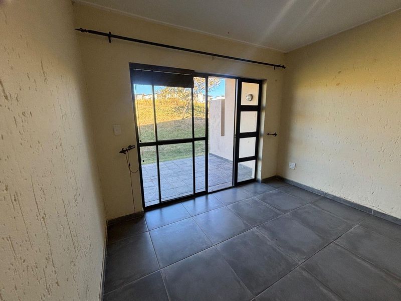 An empty living room featuring dark floor tiles, textured walls, and a sliding glass door providing direct access to an outdoor patio area.