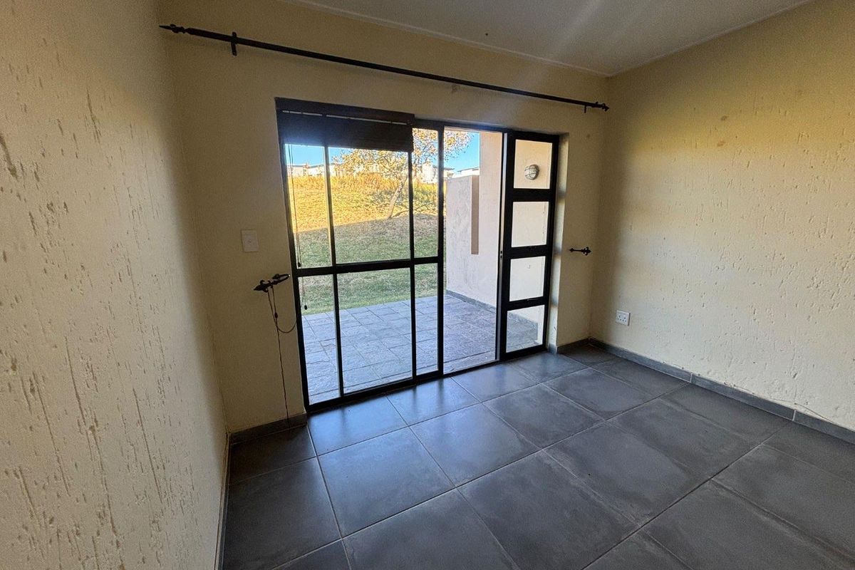An empty living room featuring dark floor tiles, textured walls, and a sliding glass door providing direct access to an outdoor patio area.