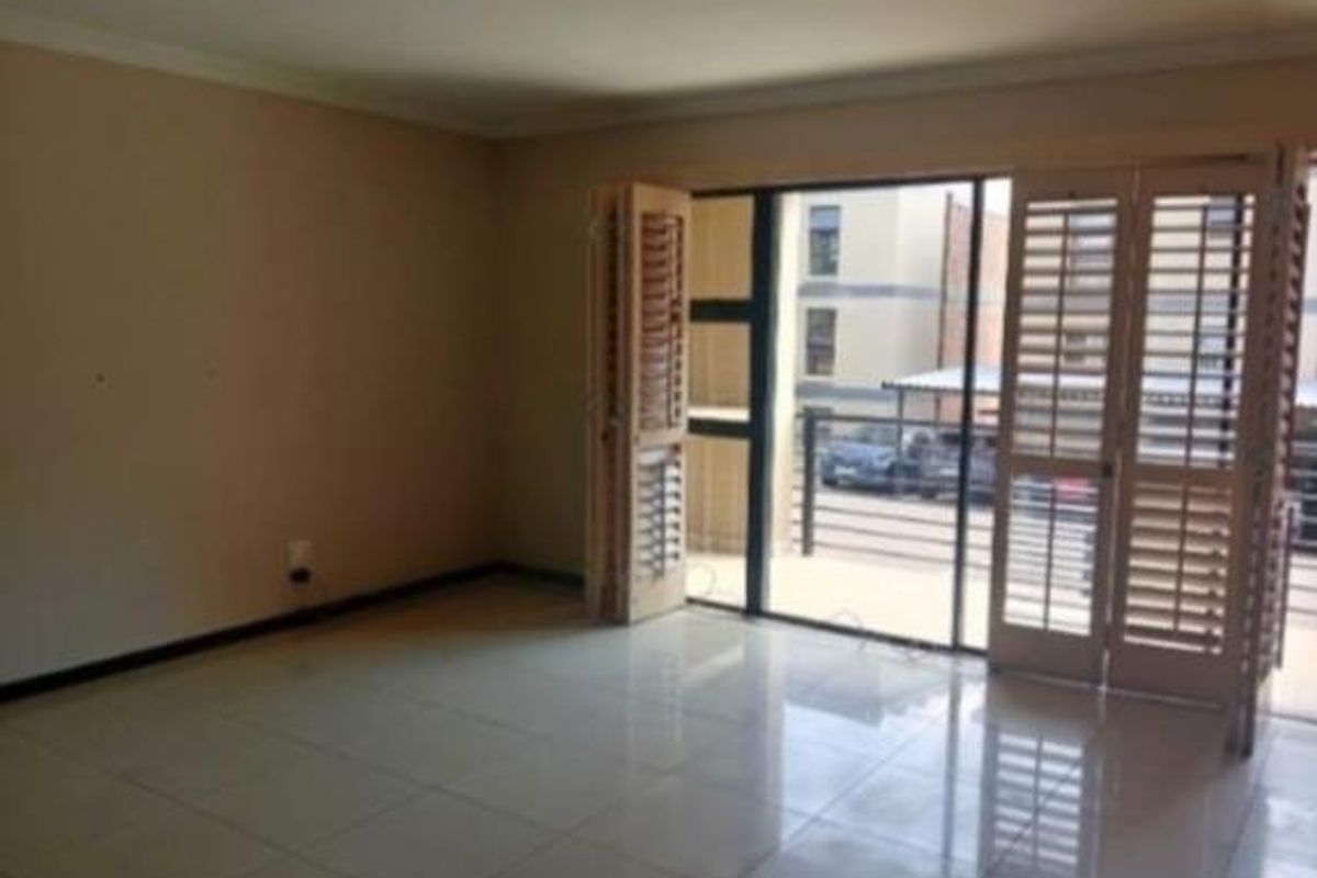 An empty living room featuring tiled flooring and plantation shutters opening onto a balcony area.
