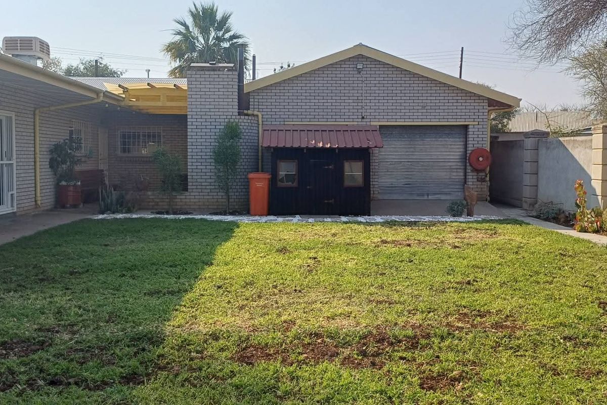 Rear view of the property featuring a brick facade, a roll-up garage door, a covered patio area, and a private garden space.