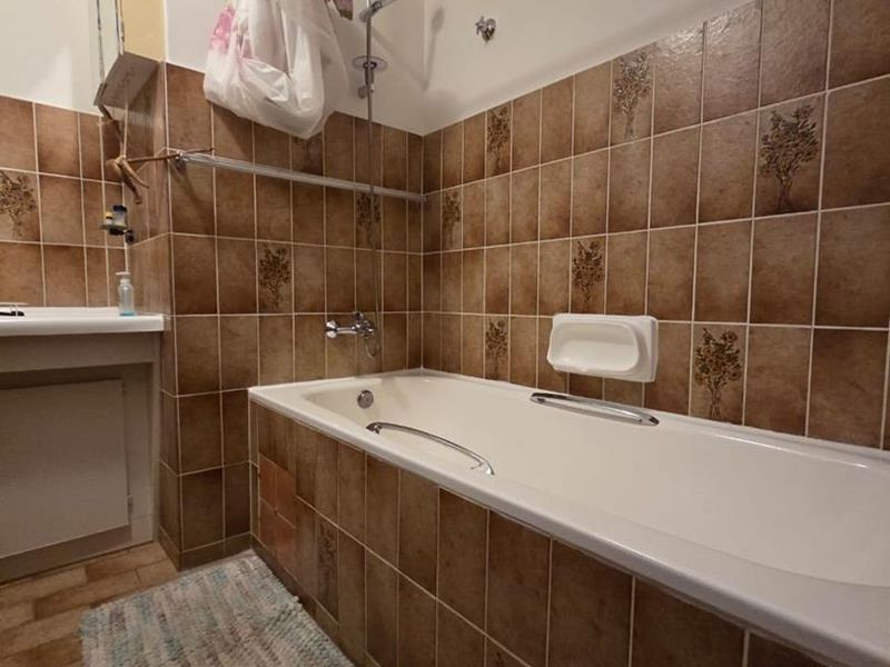 A functional bathroom featuring a built-in bathtub with shower mixer, tiled walls, and tiled flooring, offering a dated aesthetic ready for modernization.