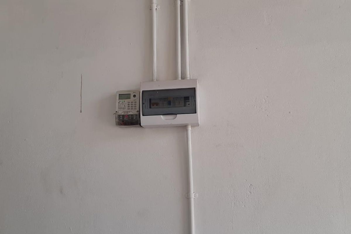 A utility wall featuring a mounted electrical distribution board and electricity meter with surface-mounted conduit piping.