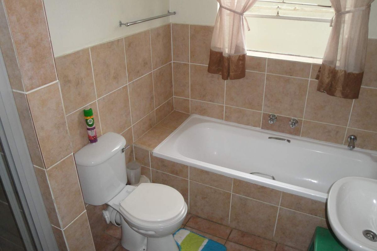A functional bathroom featuring a built-in bathtub, pedestal basin, and toilet with neutral wall and floor tiling.