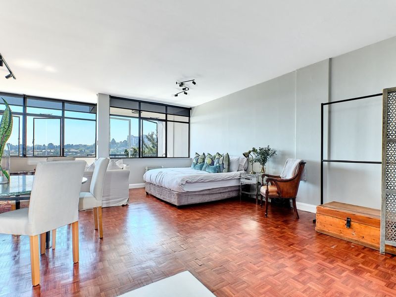 Spacious open-plan living and bedroom area featuring classic parquet flooring, large windows with natural light, and modern track lighting.