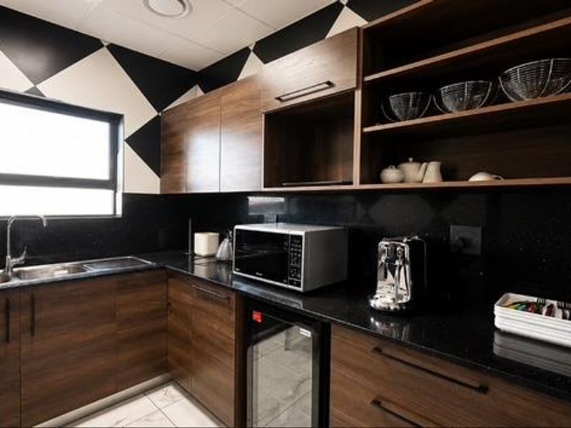 Modern kitchen featuring dark wood cabinetry, granite countertops, stainless steel sink, and integrated appliances with a striking geometric wall pattern.
