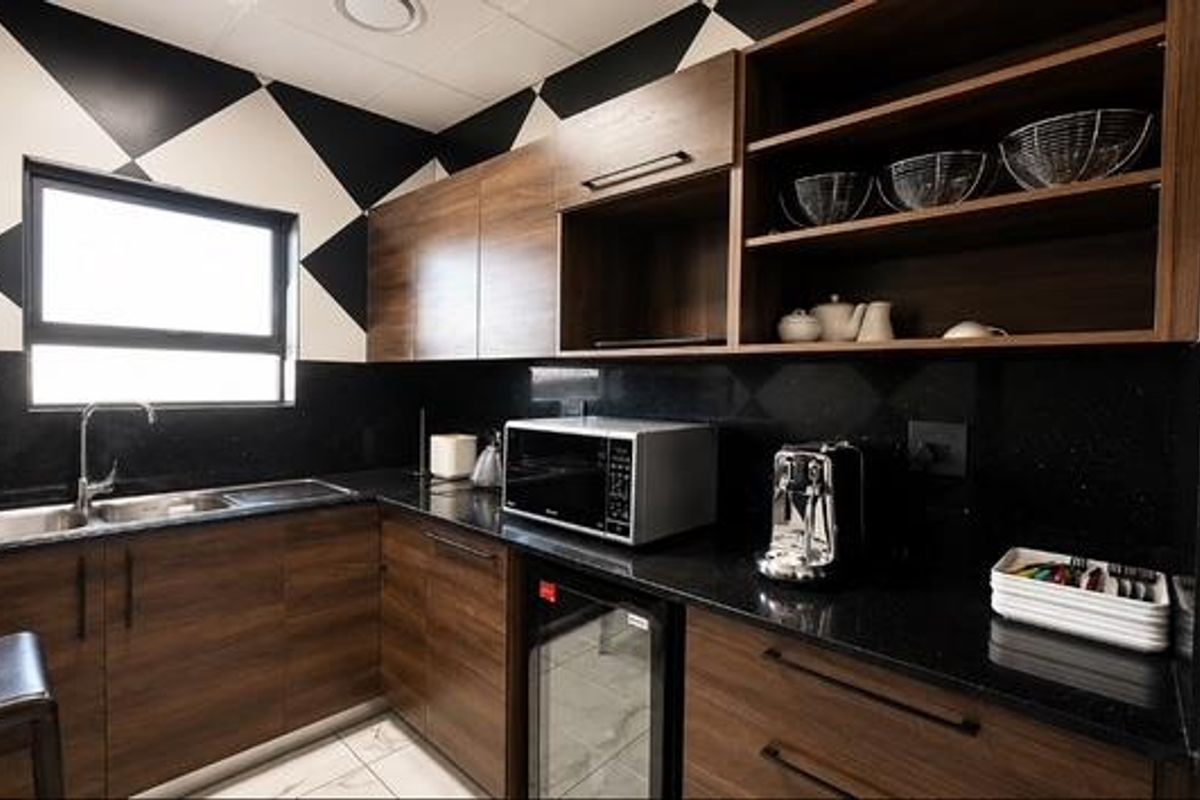 Modern kitchen featuring dark wood cabinetry, granite countertops, stainless steel sink, and integrated appliances with a striking geometric wall pattern.