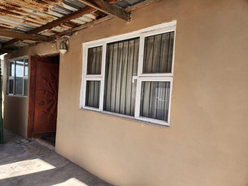 Covered patio area featuring a corrugated iron roof with timber rafters, solid timber door, and aluminium windows with security bars.