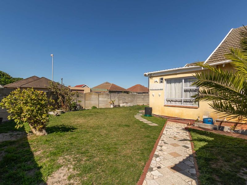 Rear garden area featuring a lawn, paved walkway, and precast concrete boundary wall, with visible exterior wall maintenance required.