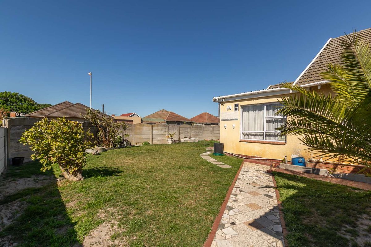 Rear garden area featuring a lawn, paved walkway, and precast concrete boundary wall, with visible exterior wall maintenance required.