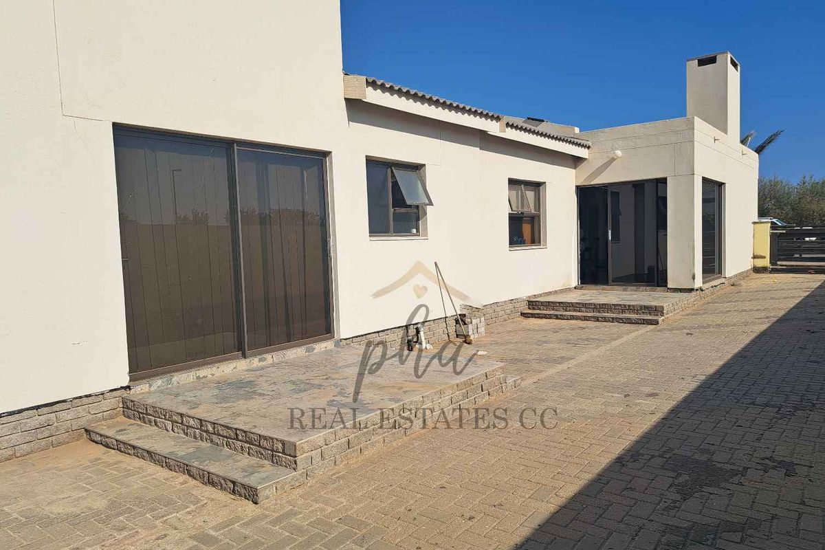 Rear exterior view of the house featuring a paved patio area, sliding glass doors, and a built-in chimney structure.
