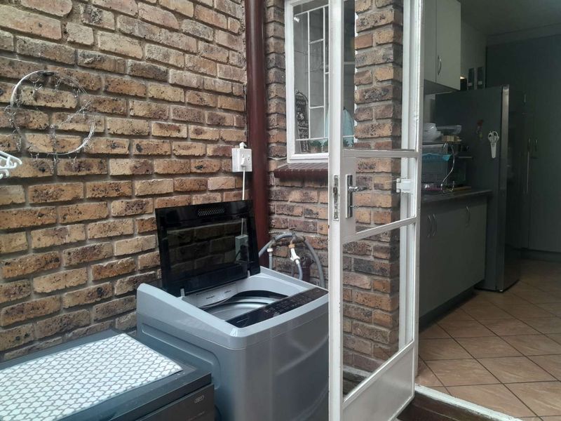 Outdoor laundry area featuring exposed brick walls and direct access to the kitchen, equipped with plumbing connections for a washing machine.
