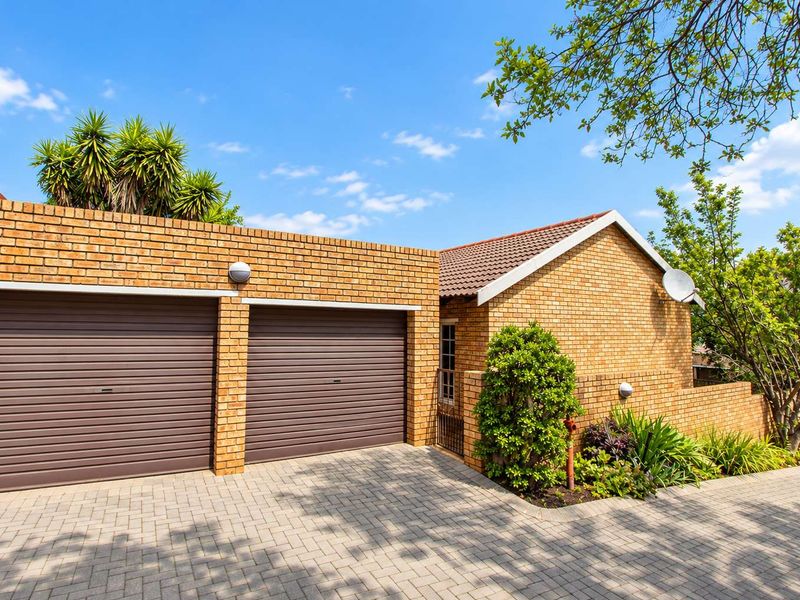 A well-maintained townhouse exterior featuring a double garage with roller doors, brick facade, and a paved driveway.