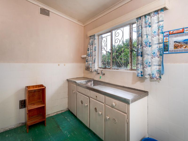 A functional scullery area featuring a stainless steel sink, built-in cabinetry, and tiled splashbacks, requiring cosmetic updates to modernize the space.