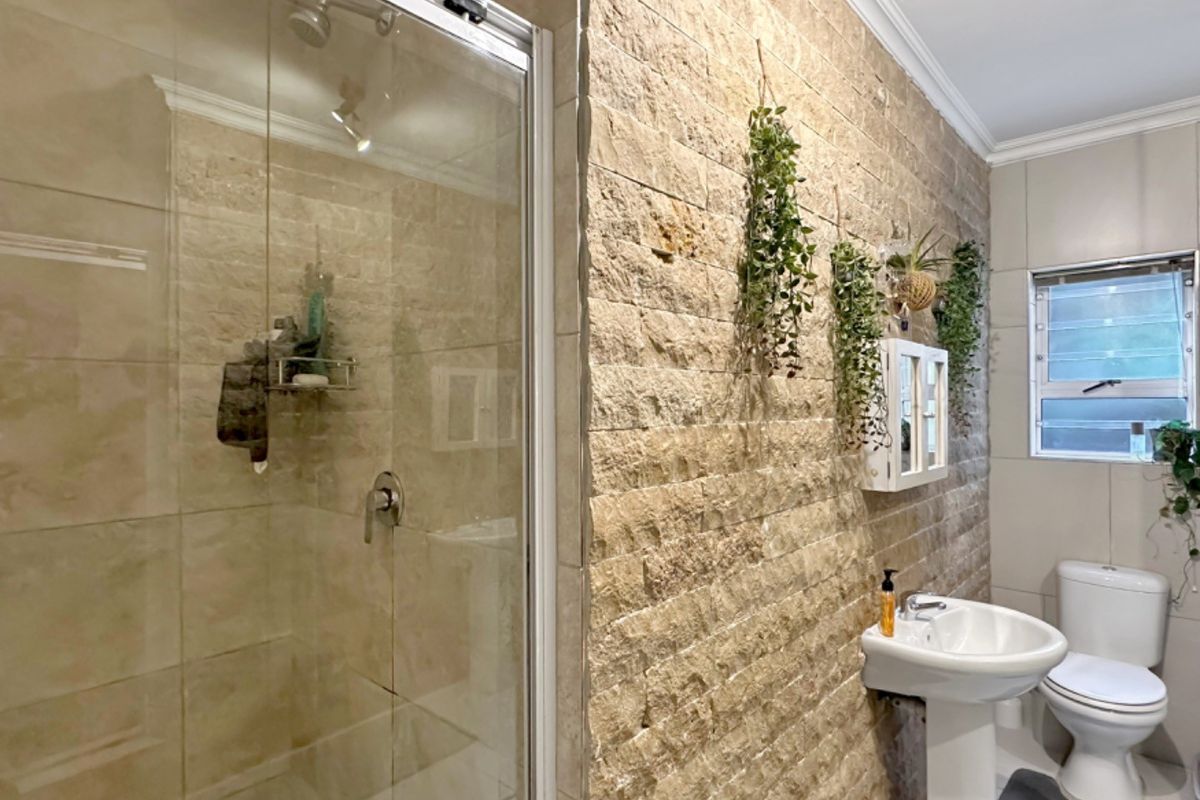 Modern bathroom featuring a glass-enclosed shower, pedestal sink, toilet, and a distinctive textured stone feature wall.