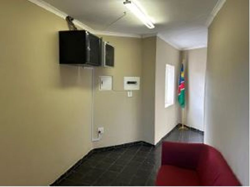 A functional office space featuring tiled flooring, a wall-mounted electrical distribution board, and overhead fluorescent lighting.