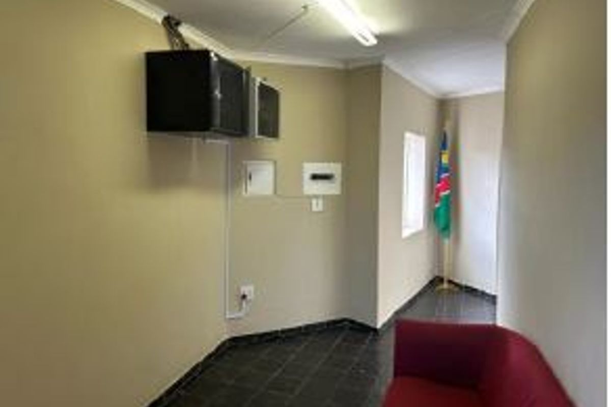 A functional office space featuring tiled flooring, a wall-mounted electrical distribution board, and overhead fluorescent lighting.