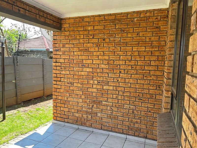 A covered patio area featuring face brick walls and tiled flooring, providing a functional outdoor space overlooking the garden.
