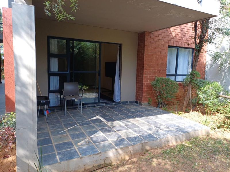 A covered ground-floor patio featuring dark tiled flooring, exposed brickwork, and sliding glass door access to the interior living space.
