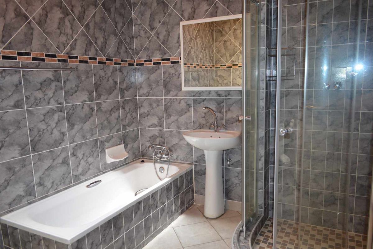A functional bathroom featuring a pedestal basin, a built-in bathtub, and a separate glass-enclosed shower with grey marble-effect wall tiling.