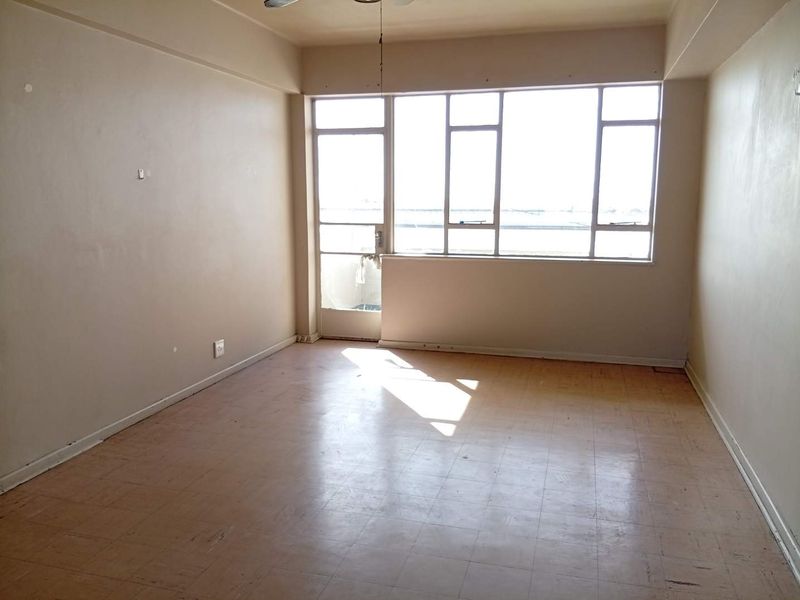 An empty living room featuring large windows, a ceiling fan, and vinyl tile flooring, offering a blank canvas for renovation.