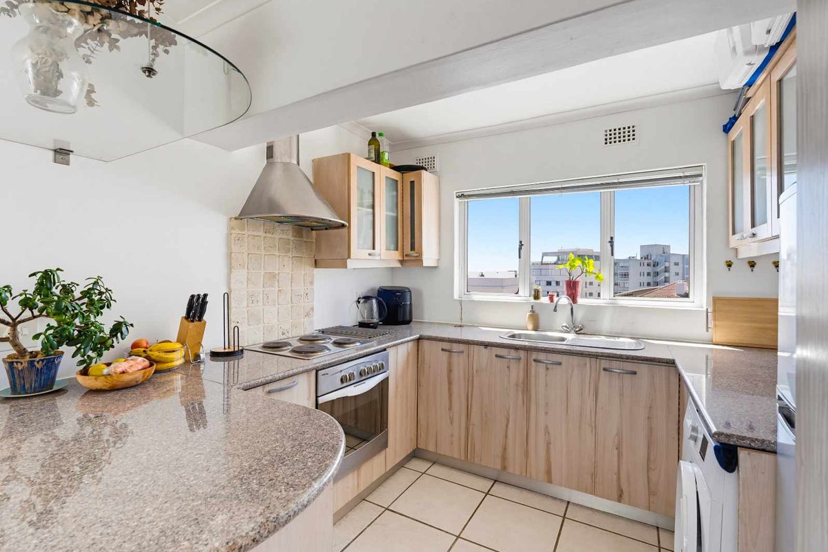 A functional kitchen featuring granite countertops, light wood cabinetry, built-in oven and hob, and a tiled backsplash with a view through the window.