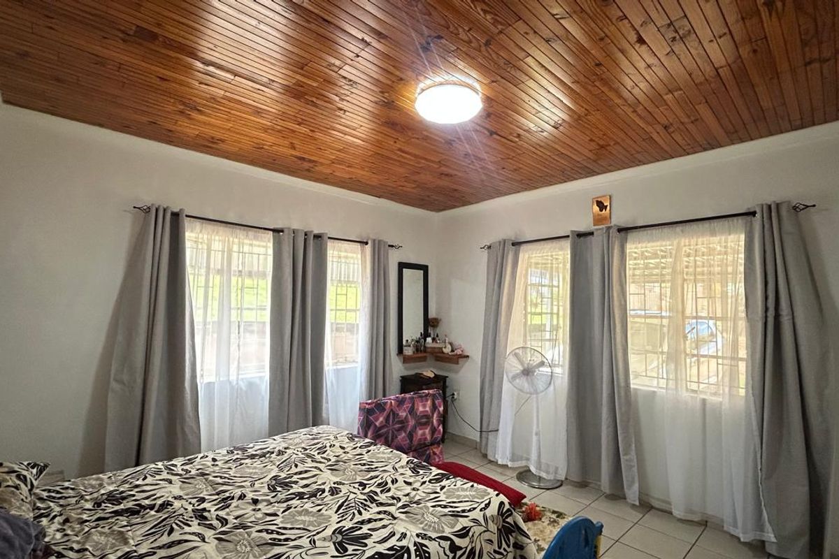 A bedroom featuring a distinctive timber-paneled ceiling, tiled flooring, and large windows that provide ample natural light.