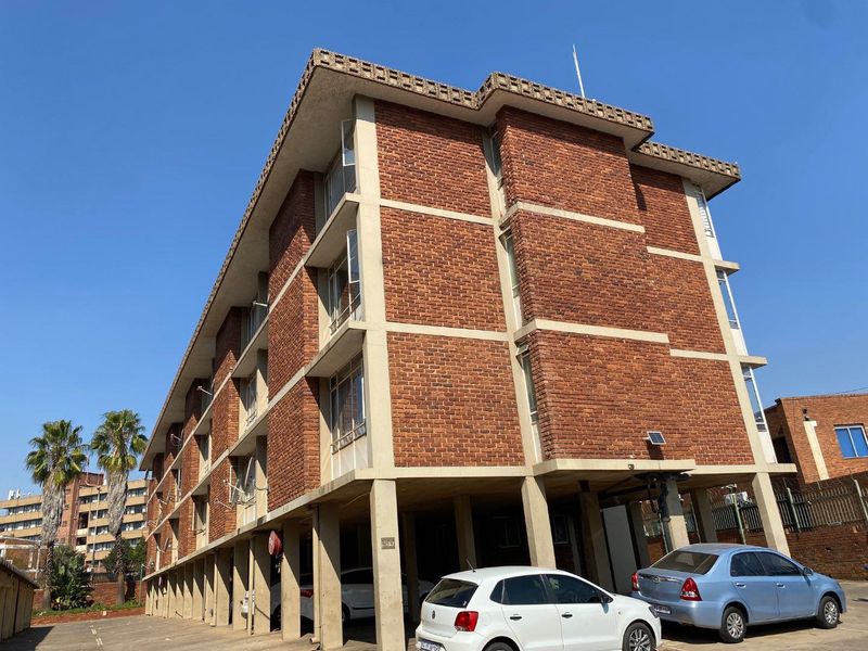 Exterior view of a multi-story apartment building featuring exposed brick facade, concrete structural columns, and covered ground-level parking area.