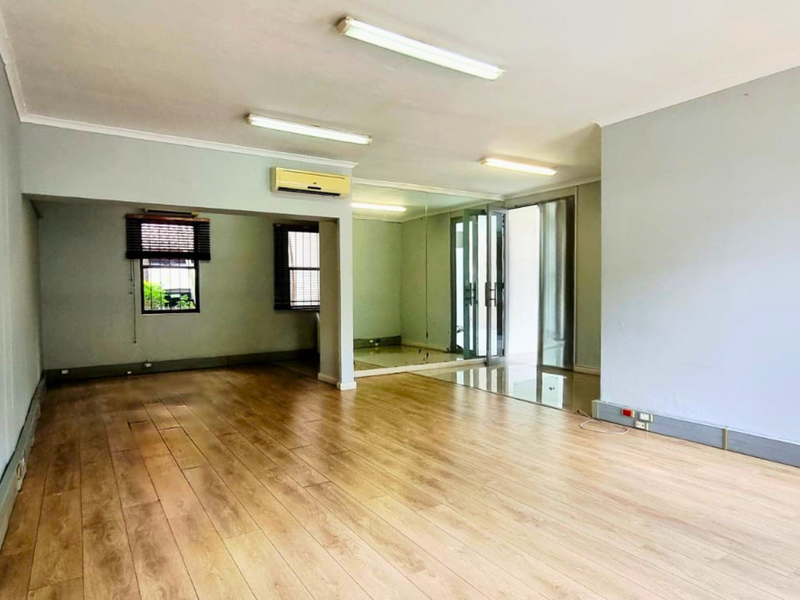 Spacious, empty office area featuring laminate flooring, mirrored wall accents, and wall-mounted air conditioning, providing a clean and versatile workspace.