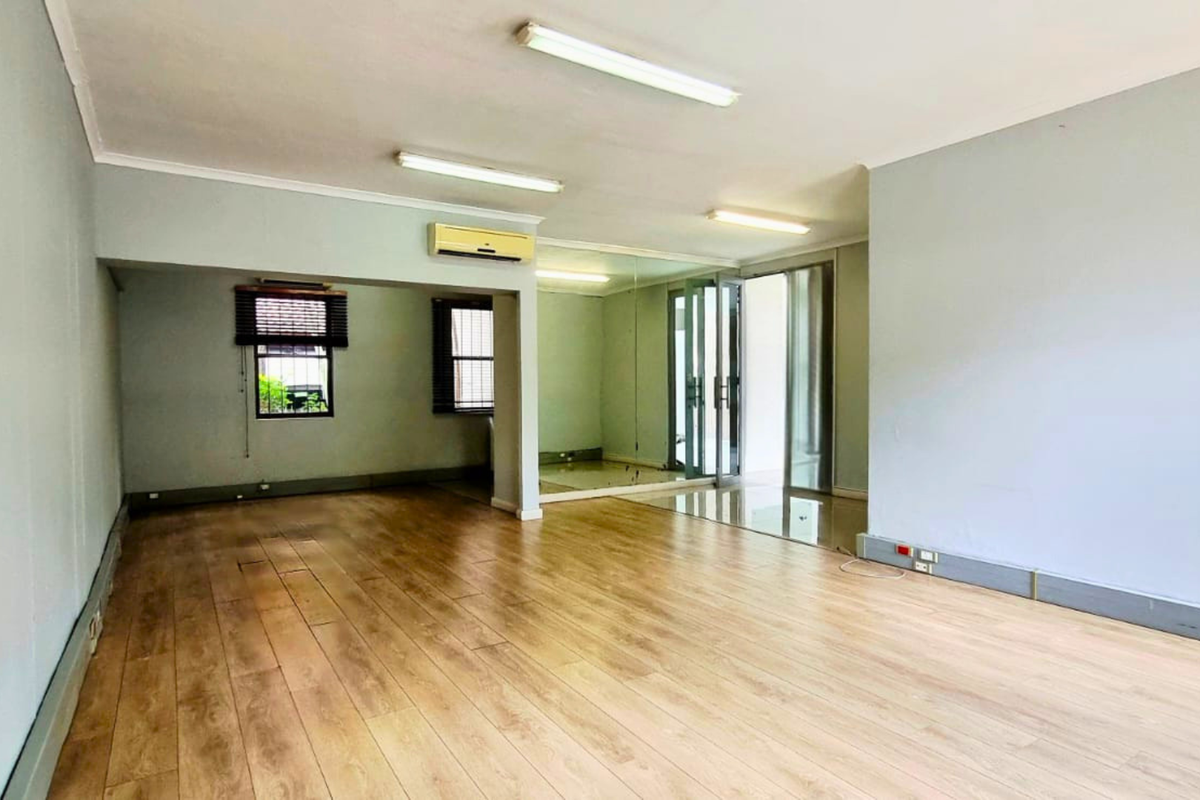 Spacious, empty office area featuring laminate flooring, mirrored wall accents, and wall-mounted air conditioning, providing a clean and versatile workspace.
