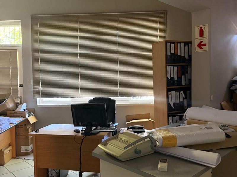 A functional office space featuring tiled flooring, venetian blinds, and a wall-mounted air conditioning unit.