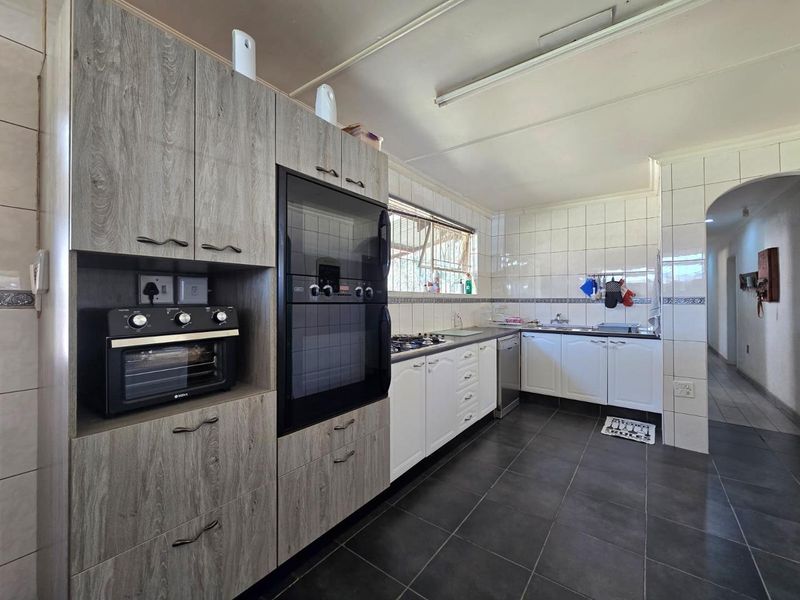 A functional kitchen featuring modern grey wood-look cabinetry, a built-in oven, gas hob, and tiled finishes throughout.
