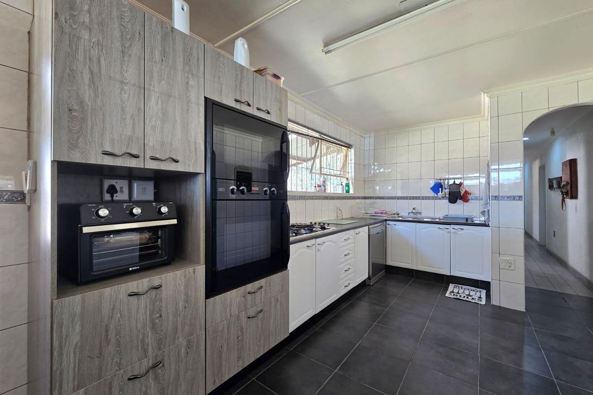A functional kitchen featuring modern grey wood-look cabinetry, a built-in oven, gas hob, and tiled finishes throughout.