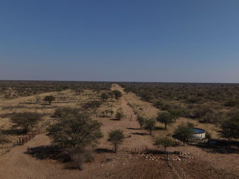 Aerial view of the expansive farm property featuring a water reservoir, perimeter fencing, and a central dirt access track.