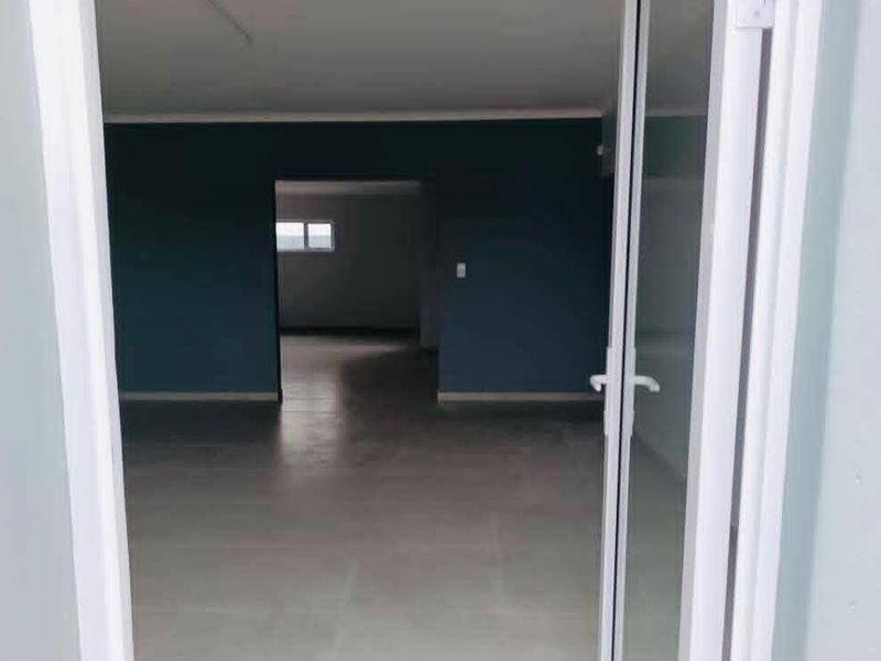 An empty, open-plan living area featuring tiled flooring and a sliding glass door entrance, finished with dark blue accent walls.