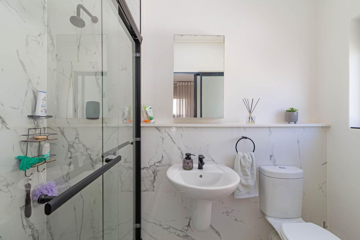 Modern bathroom featuring a glass-enclosed shower with marble-look wall tiles, a pedestal basin, and a wall-mounted mirror.