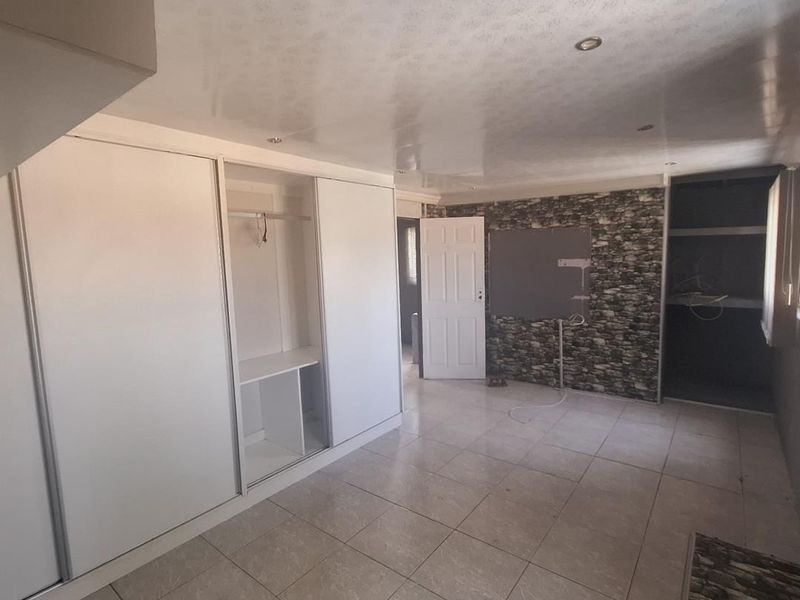 An empty bedroom featuring built-in sliding wardrobes, tiled flooring, and recessed ceiling lights, offering a blank canvas for potential renovation.