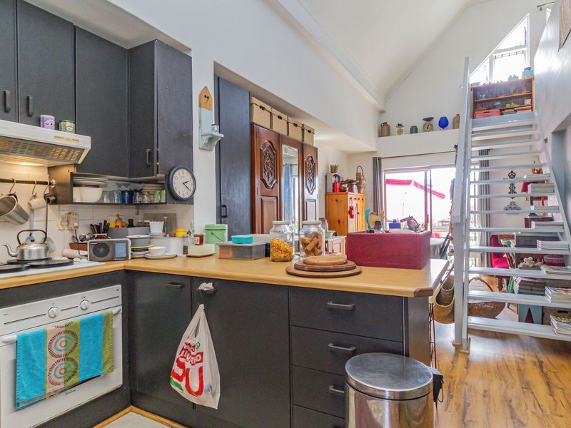 Open plan kitchen area featuring dark cabinetry, light wood countertops, and a staircase leading to a mezzanine level under a vaulted ceiling.