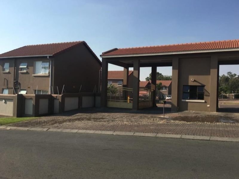 Front exterior view of the apartment complex entrance featuring a security gate, guard house, and paved driveway with electric fencing.