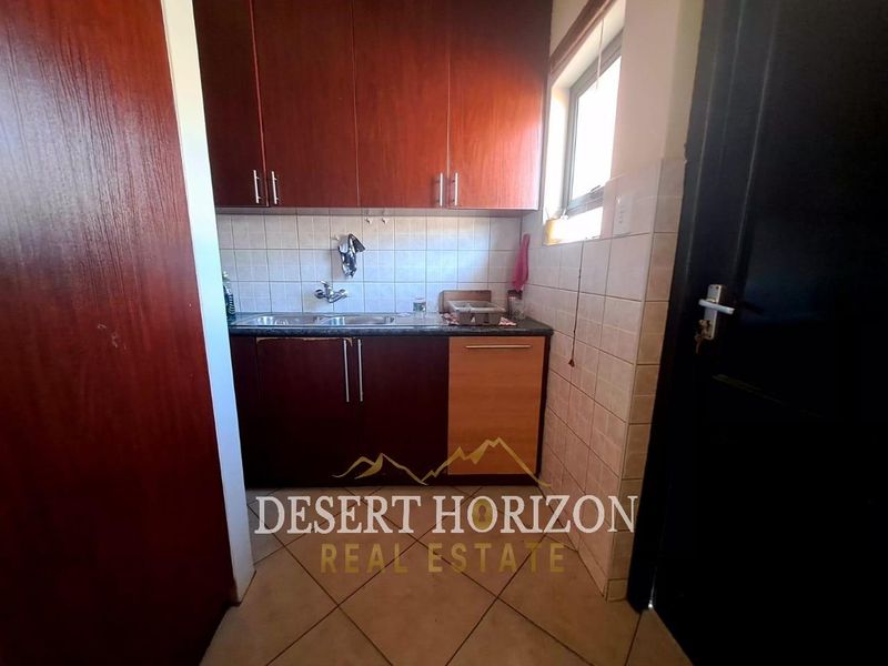 A compact scullery area featuring built-in cabinetry, a stainless steel sink, and tiled finishes, providing functional utility space.