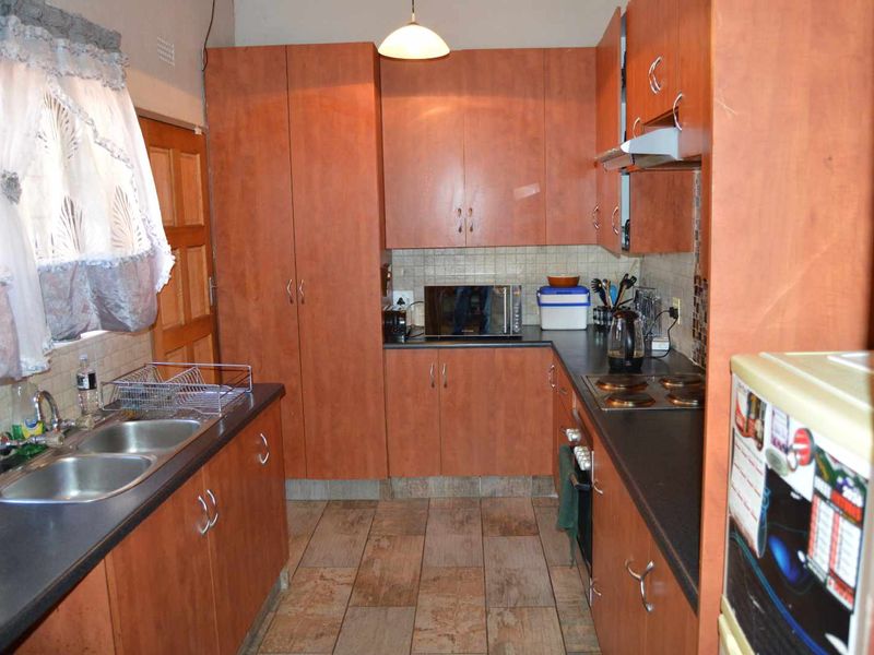 A functional kitchen featuring laminate cabinetry, a double bowl stainless steel sink, built-in oven, electric hob, and tiled flooring.